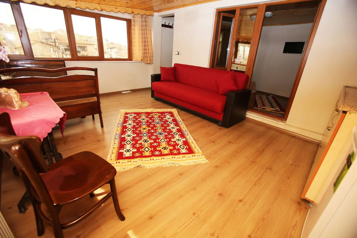 A room with a wooden floor, a red sofa, a wooden chair, a wooden bed, and a window with curtains.