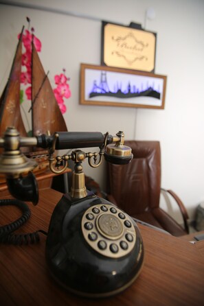 Un teléfono antiguo de disco giratorio sobre un escritorio de madera con un cuadro enmarcado y un objeto decorativo al fondo.