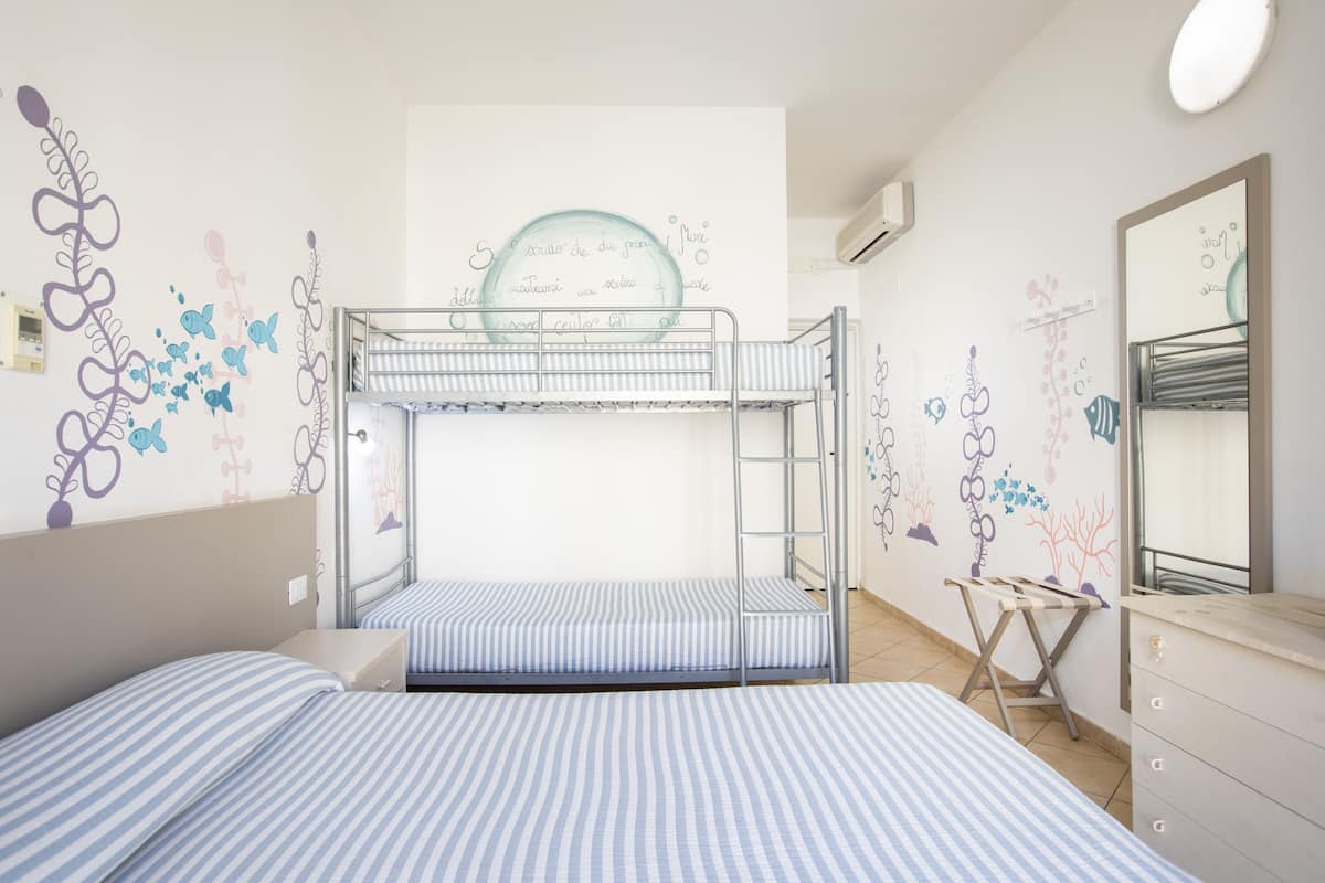 A bunk bed room with striped bedding, a ladder, a small desk, and decorative wall art.
