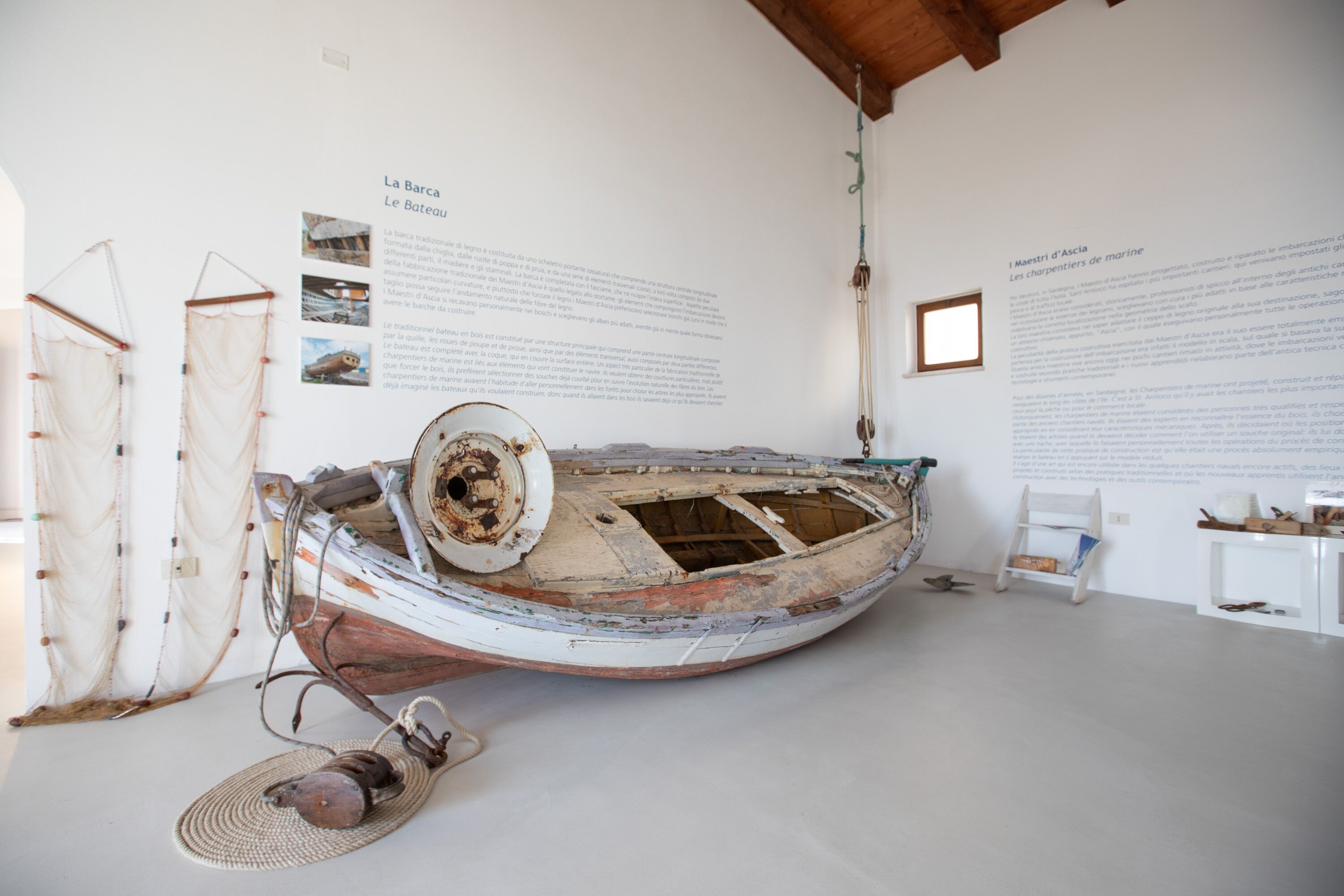 Ein Boot, das in einem Innenraum mit Infotafeln und einem kleinen Fenster präsentiert wird.