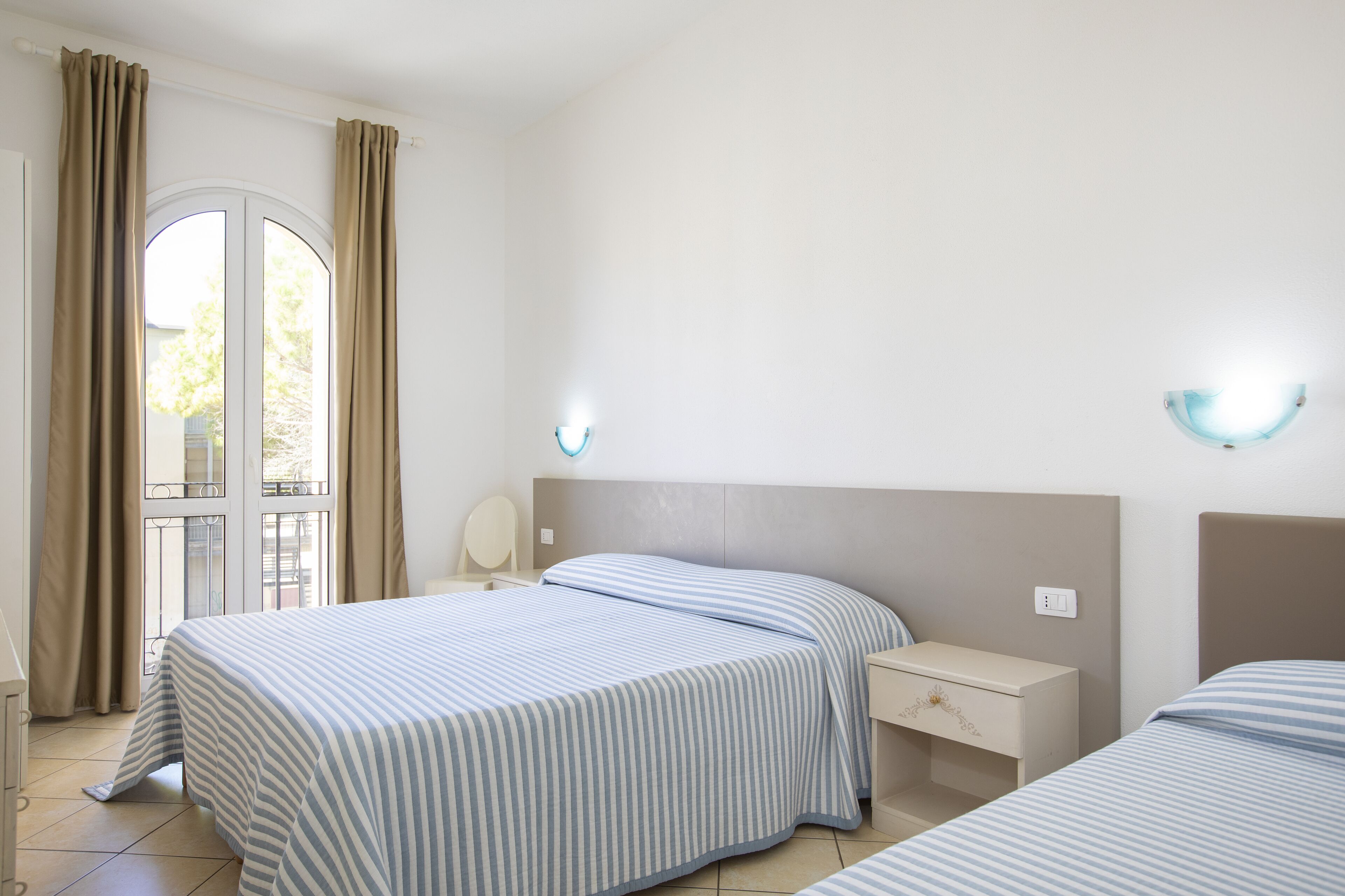 A hotel room with two beds, a nightstand, a desk, and a window with curtains.