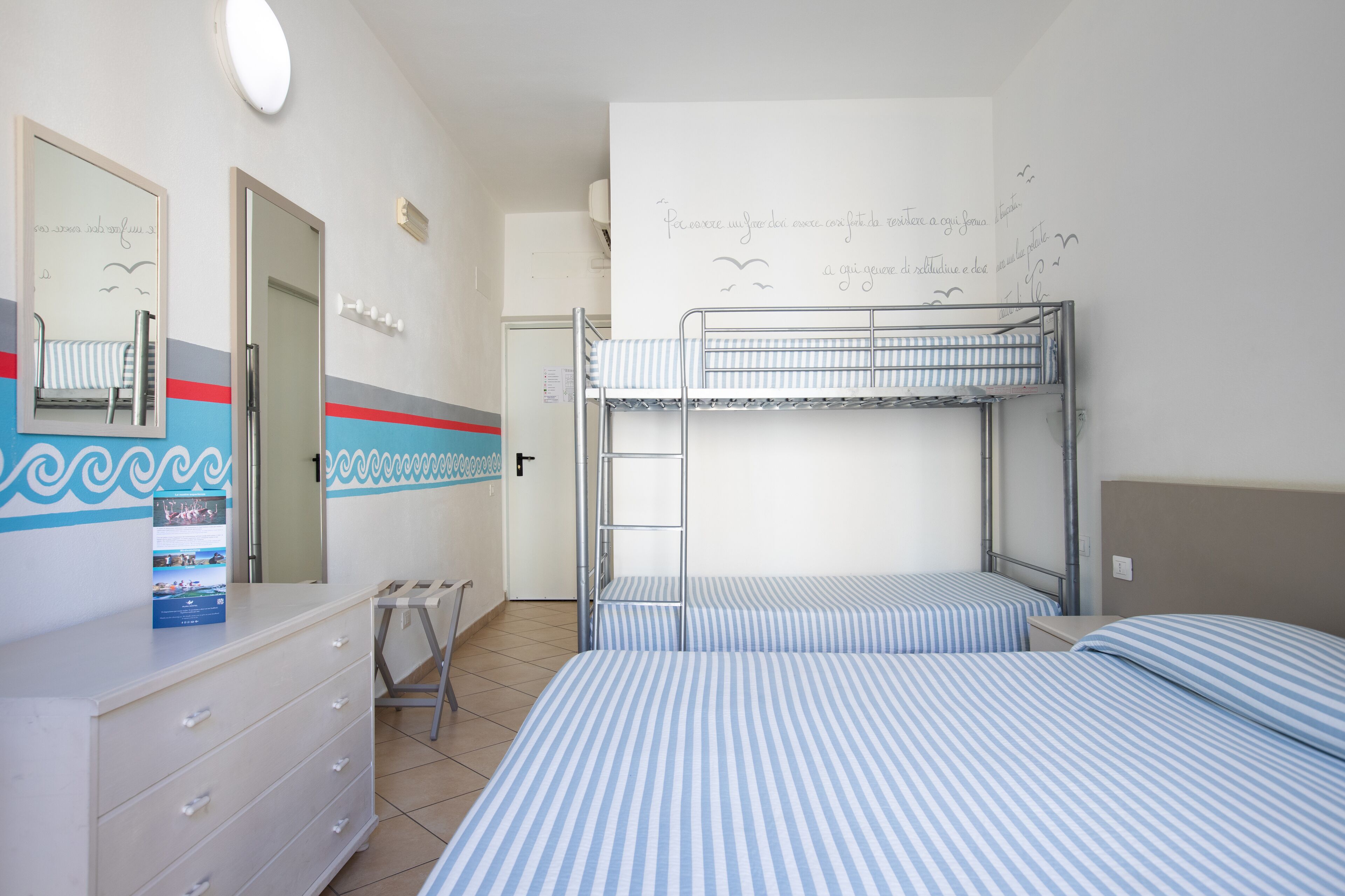 A hotel room with bunk beds, a dresser, a mirror, and a wall with decorative text and drawings.
