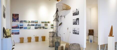 A gallery with various artworks and installations, including a large net structure, photographs on the wall, and several baskets.