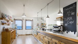 Een café met een houten toonbank, een espressoapparaat en uitzicht op zee door grote ramen.
