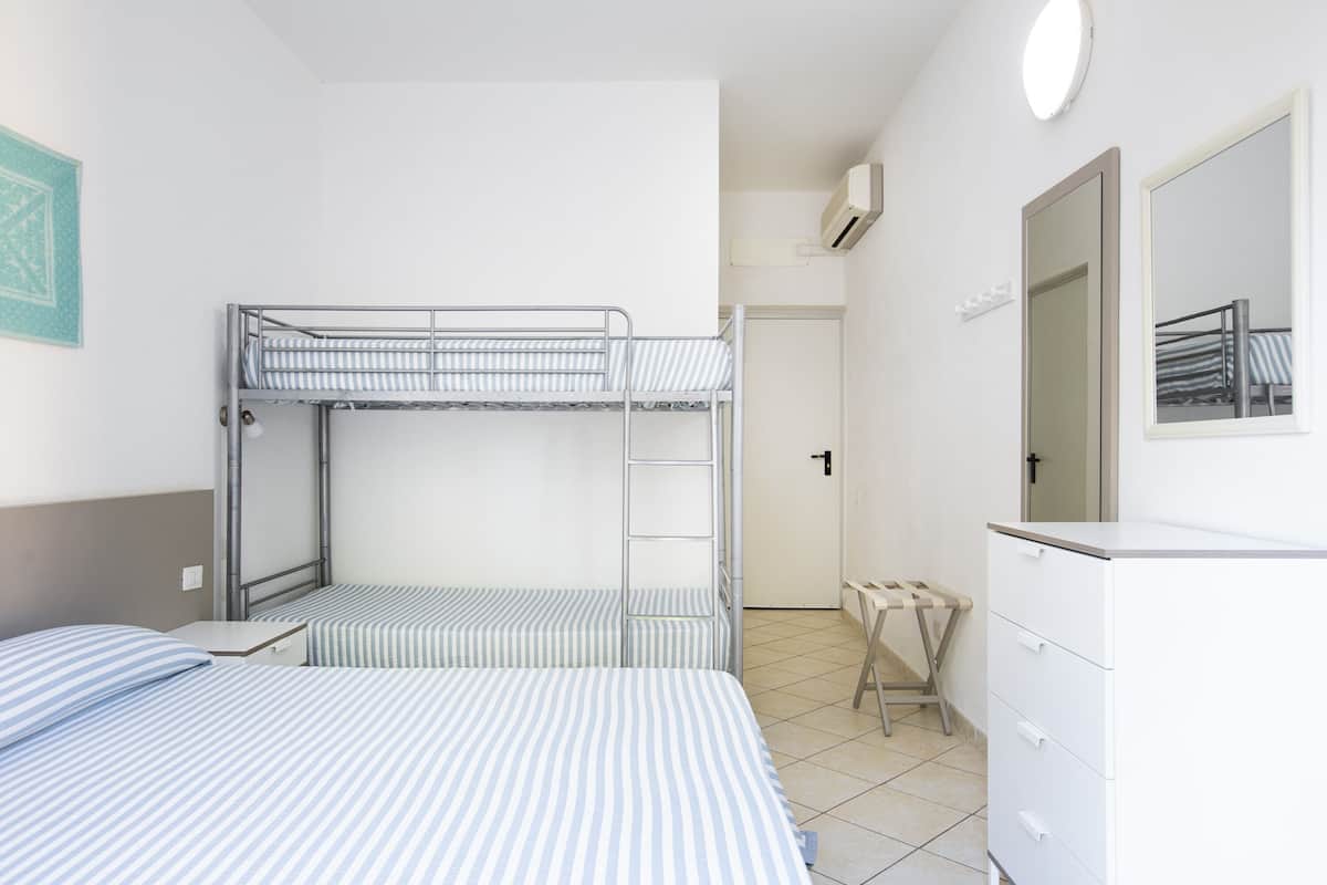 A bunk bed room with a desk and dresser, a mirror, and a door.