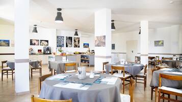 Un vaste espace dédié à la salle à manger, avec des tables rondes, des chaises et des luminaires suspendus.