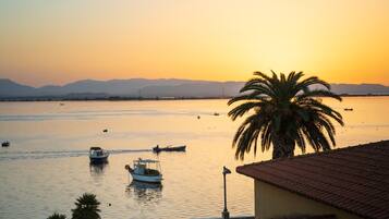 A coastal scene with boats on calm water, a palm tree, and distant mountains.