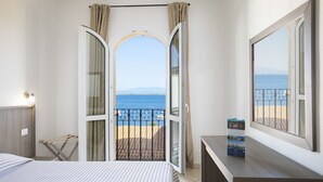 Een hotelkamer met een bed, een bureau en uitzicht op de zee door een geopende deur.
