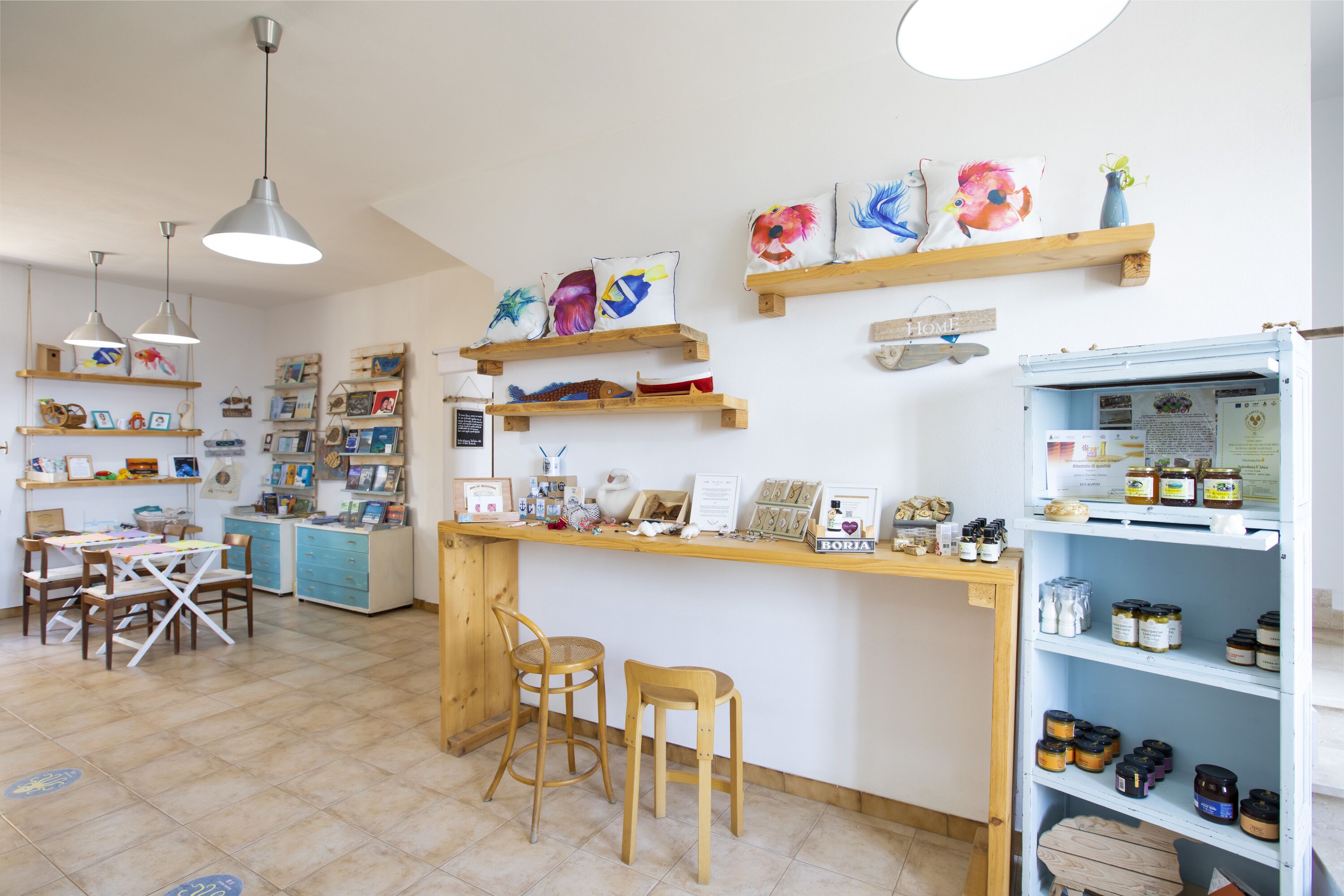 A cozy café with wooden furniture, a counter with various items, and wall decorations including fish-themed pillows.