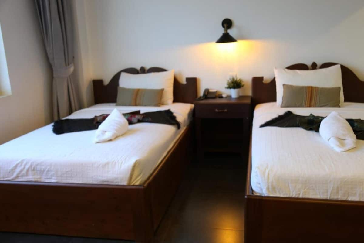 Habitación de hotel con dos camas individuales, una mesita de noche con lámpara y una pequeña planta en maceta.