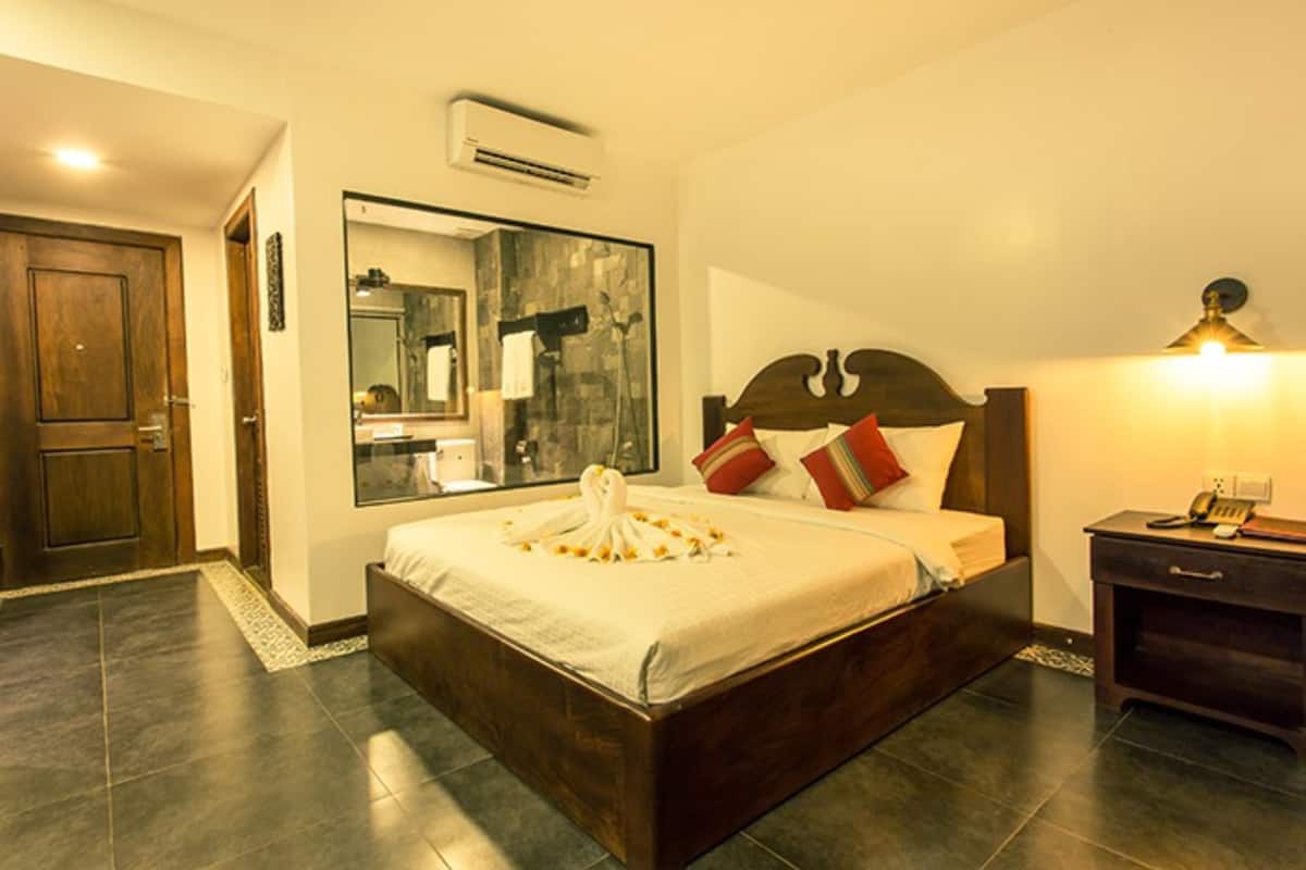 Una habitación de hotel con una cama grande, cabecera de madera, una mesita de noche, un espejo y un equipo de aire acondicionado.