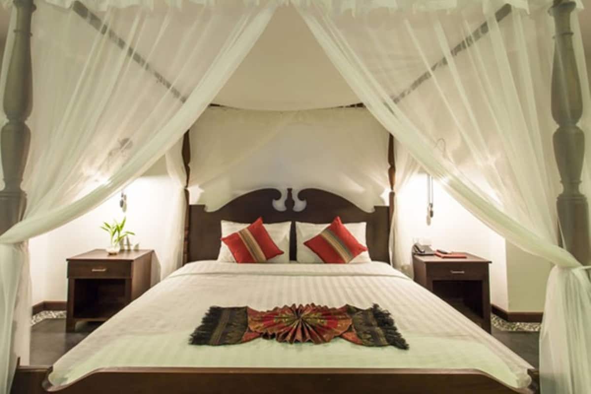 Una cama con dosel y pilares, cabecera de madera, dos mesitas de noche y un cubrelecho decorativo en la cama.