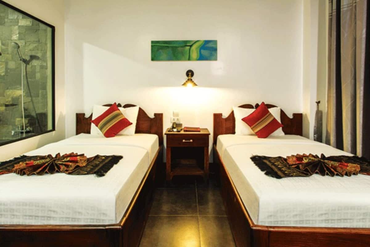 Una habitación de hotel con dos camas, una mesita de noche, una lámpara y un cuadro en la pared.