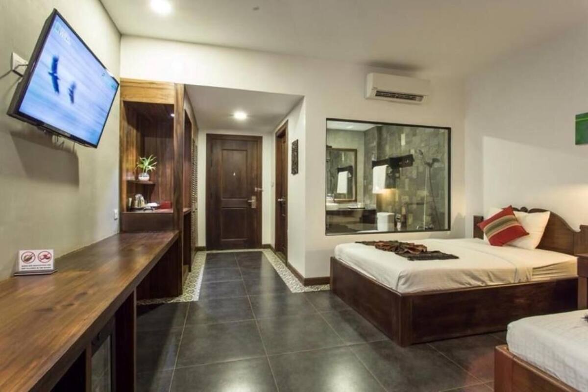 Una habitación de hotel con cama, escritorio, televisor, espejo y baño pequeño.