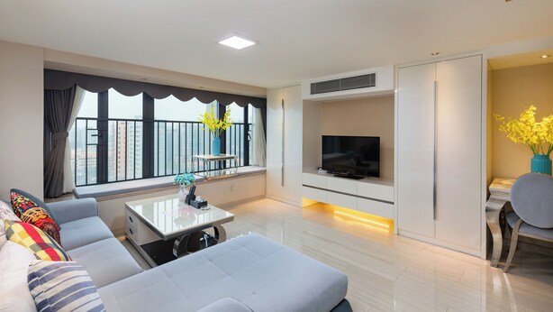 Una sala de estar moderna con un sofá, una mesa de centro, un televisor y un balcón con cortinas.