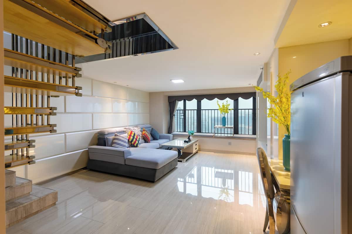 A modern living room with a grey sofa, a coffee table, and a staircase with wooden railings.