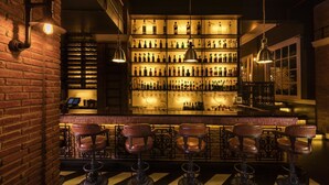 A bar area with a brick wall, multiple shelves of bottles, and leather bar stools. - Jehan Numa Palace Hotel (Bhopal)