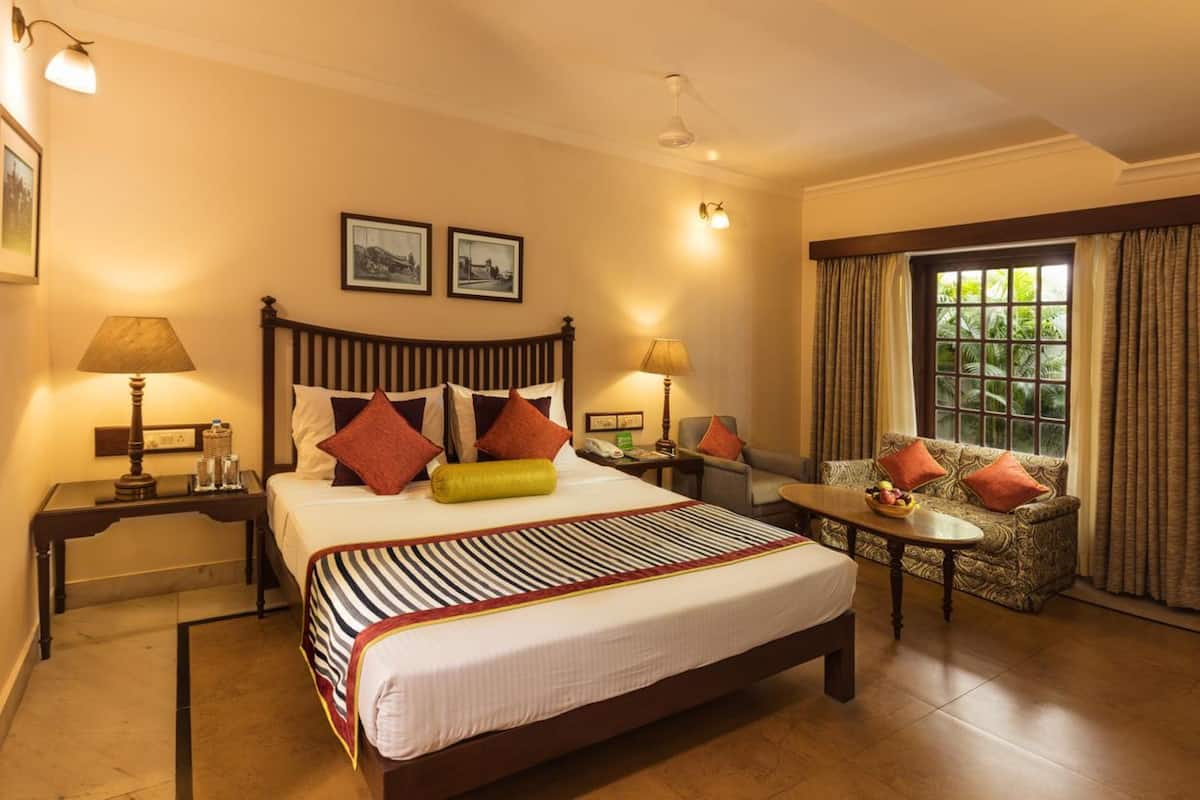 Une chambre d’hôtel avec un grand lit, deux tables de chevet, un canapé et une fenêtre avec des rideaux.