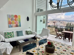 A balcony with a view of a cityscape, a white sofa with floral cushions, a wicker table, and a table with a fruit-patterned tablecloth. - Skol Apartments Marbella (Marbella)
