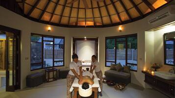 Sala de massagem com teto de madeira, janelas amplas, mesa de massagem e um sofá.