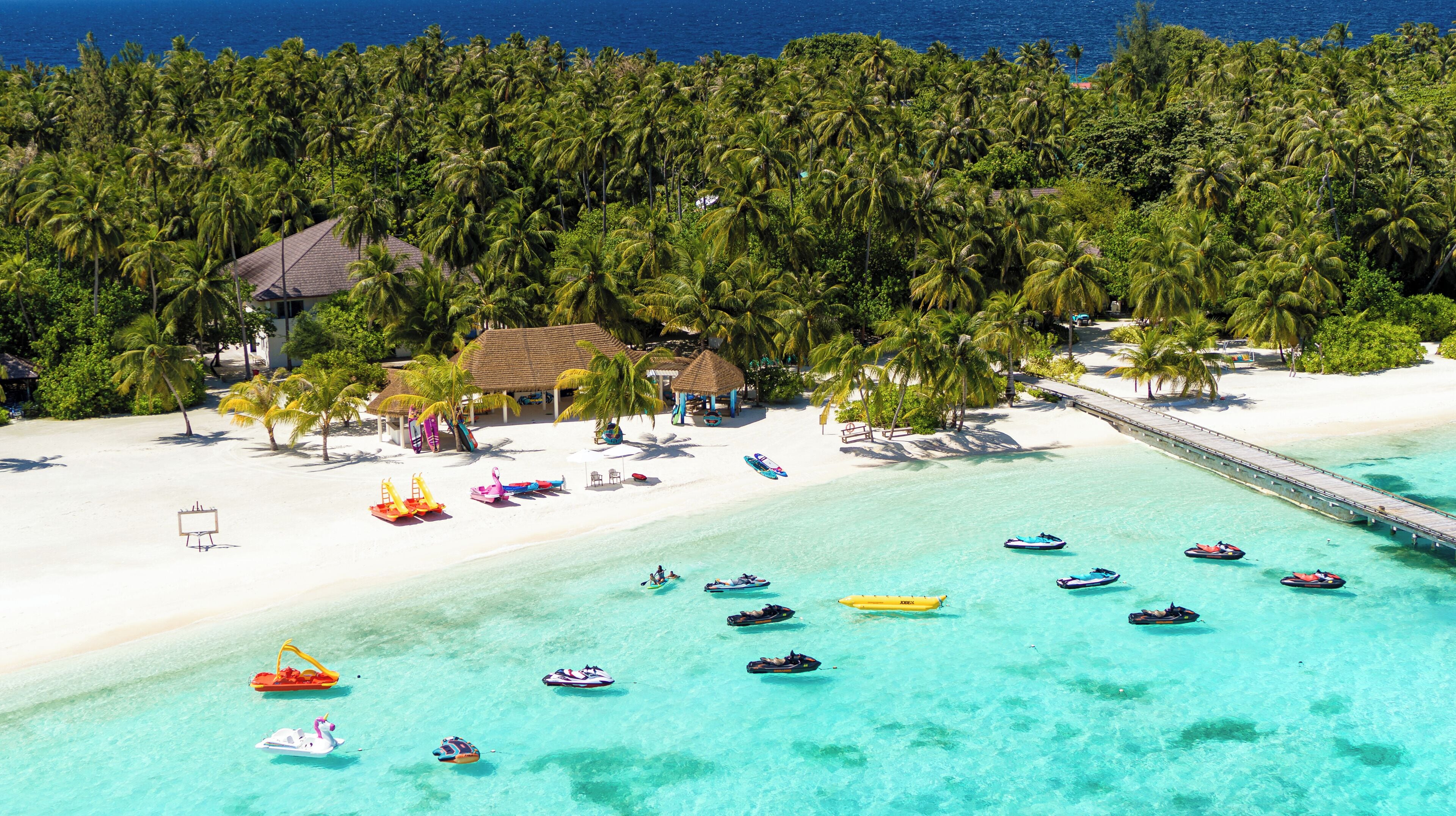 A beach resort with a white sandy beach, clear turquoise waters, and a thatched-roof hut.