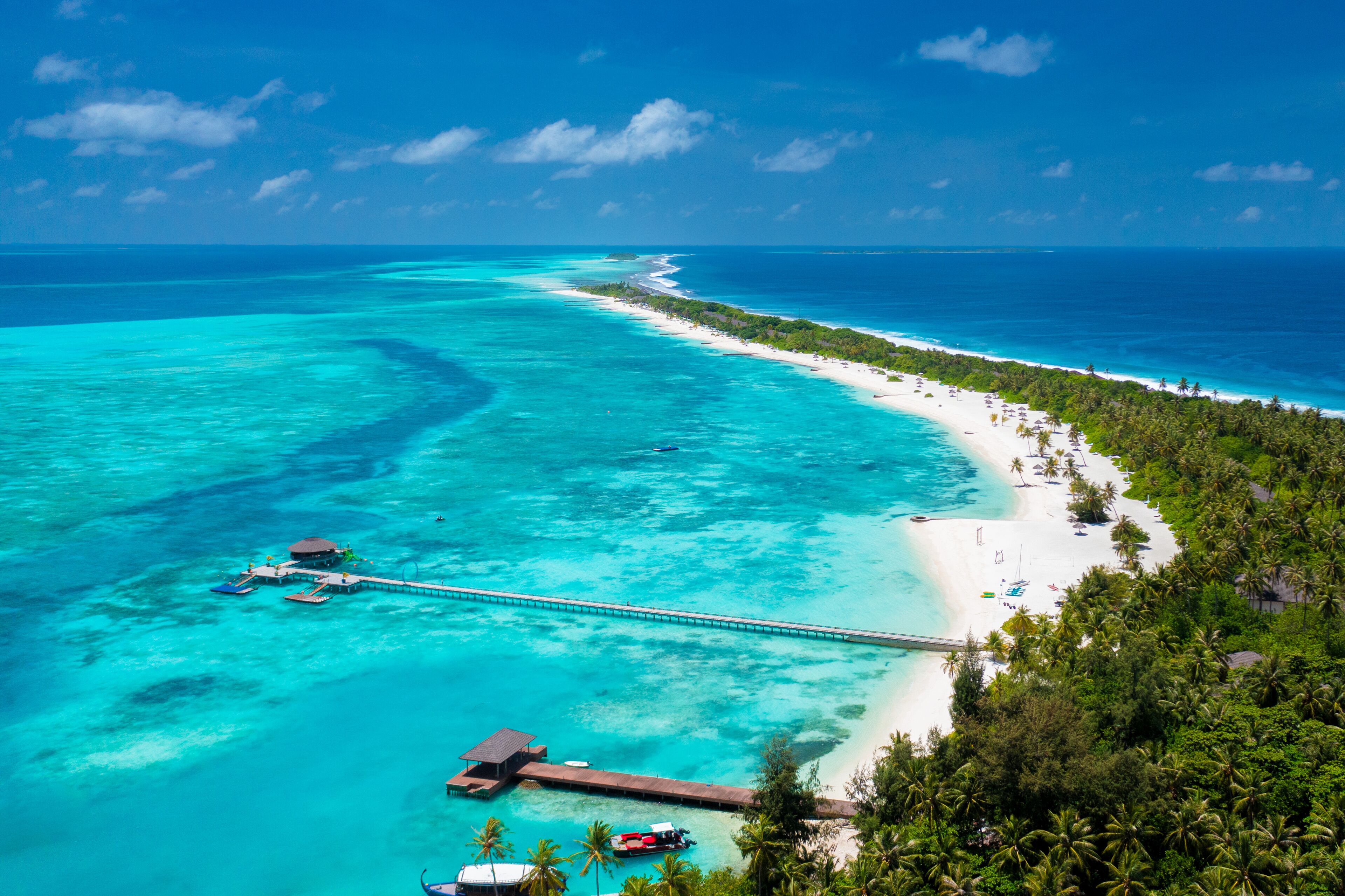 Una località balneare tropicale con una lunga banchina che si estende in acque turchesi, circondata da vegetazione lussureggiante e spiagge di sabbia bianca.