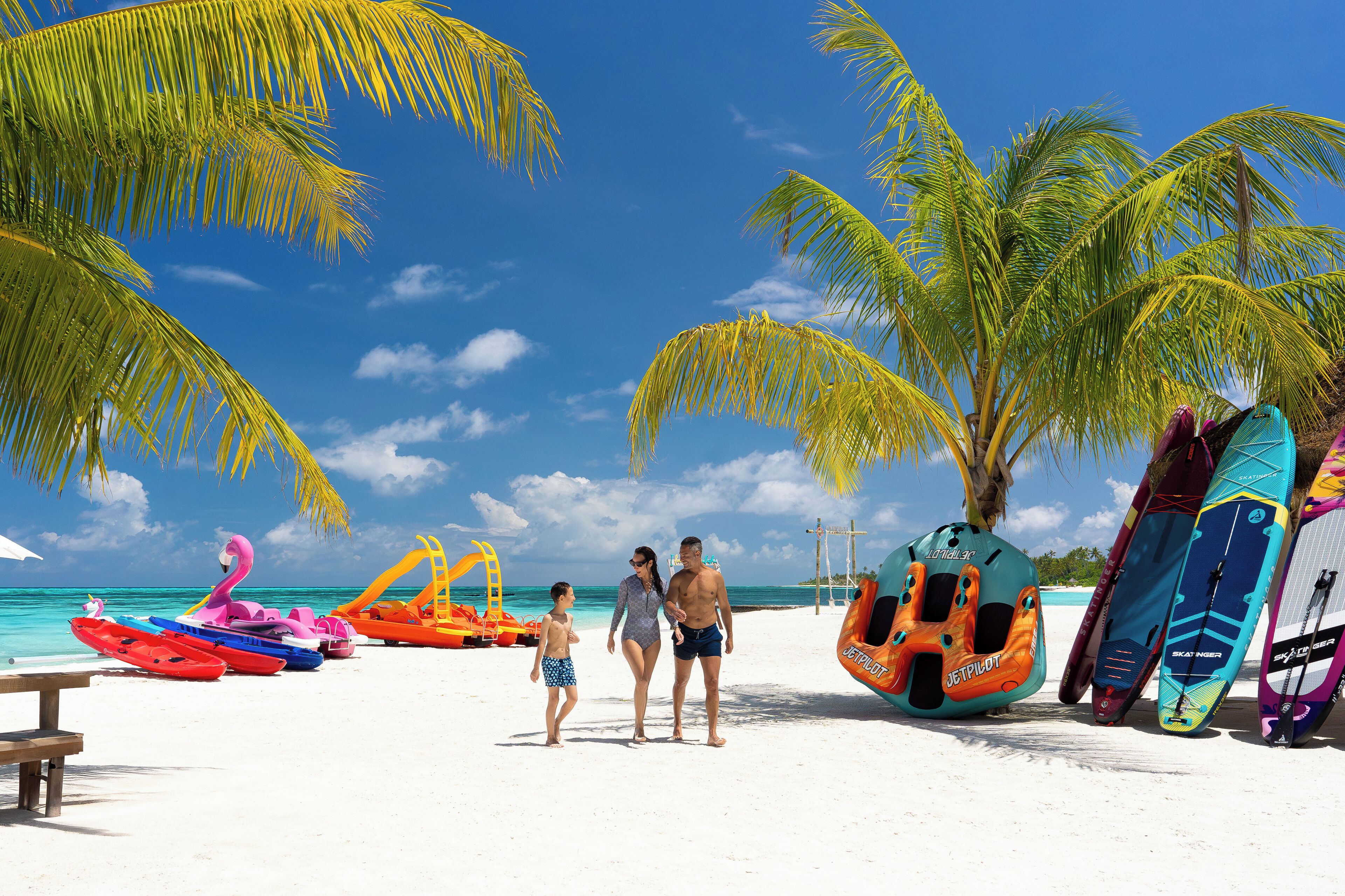 A beach with palm trees, a clear blue sky, and colorful water toys.