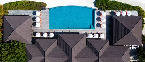 An aerial view of a hotel with a central swimming pool, multiple outdoor seating areas with umbrellas, and a symmetrical roof design.