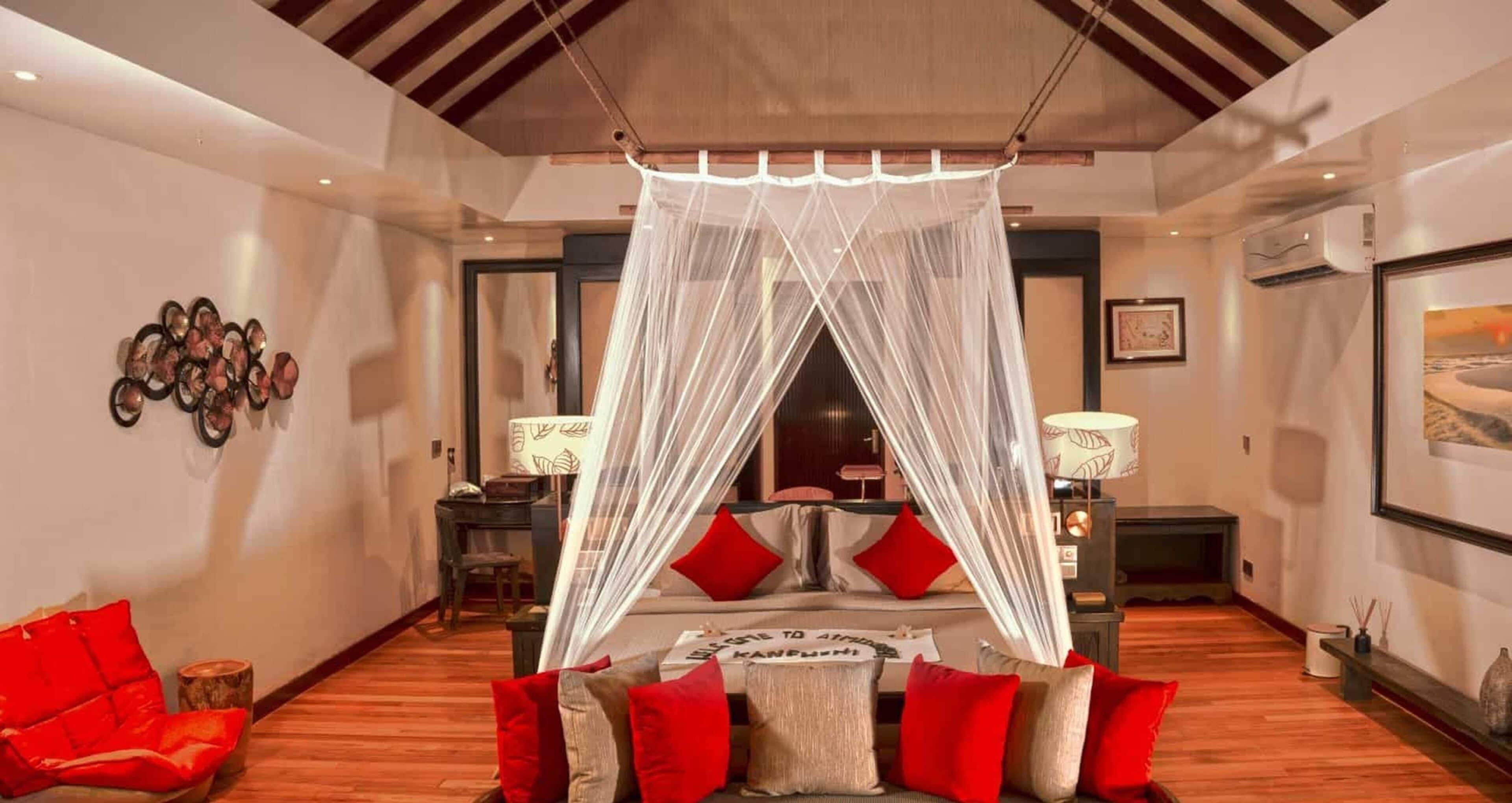 A bedroom with a canopy bed, a red sofa, and a wooden floor.