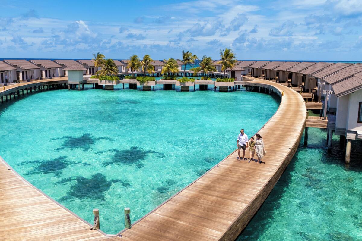 Ein Resort mit überwasserbungalows, die durch Holzstege über einer klaren, blauen Lagune verbunden sind.