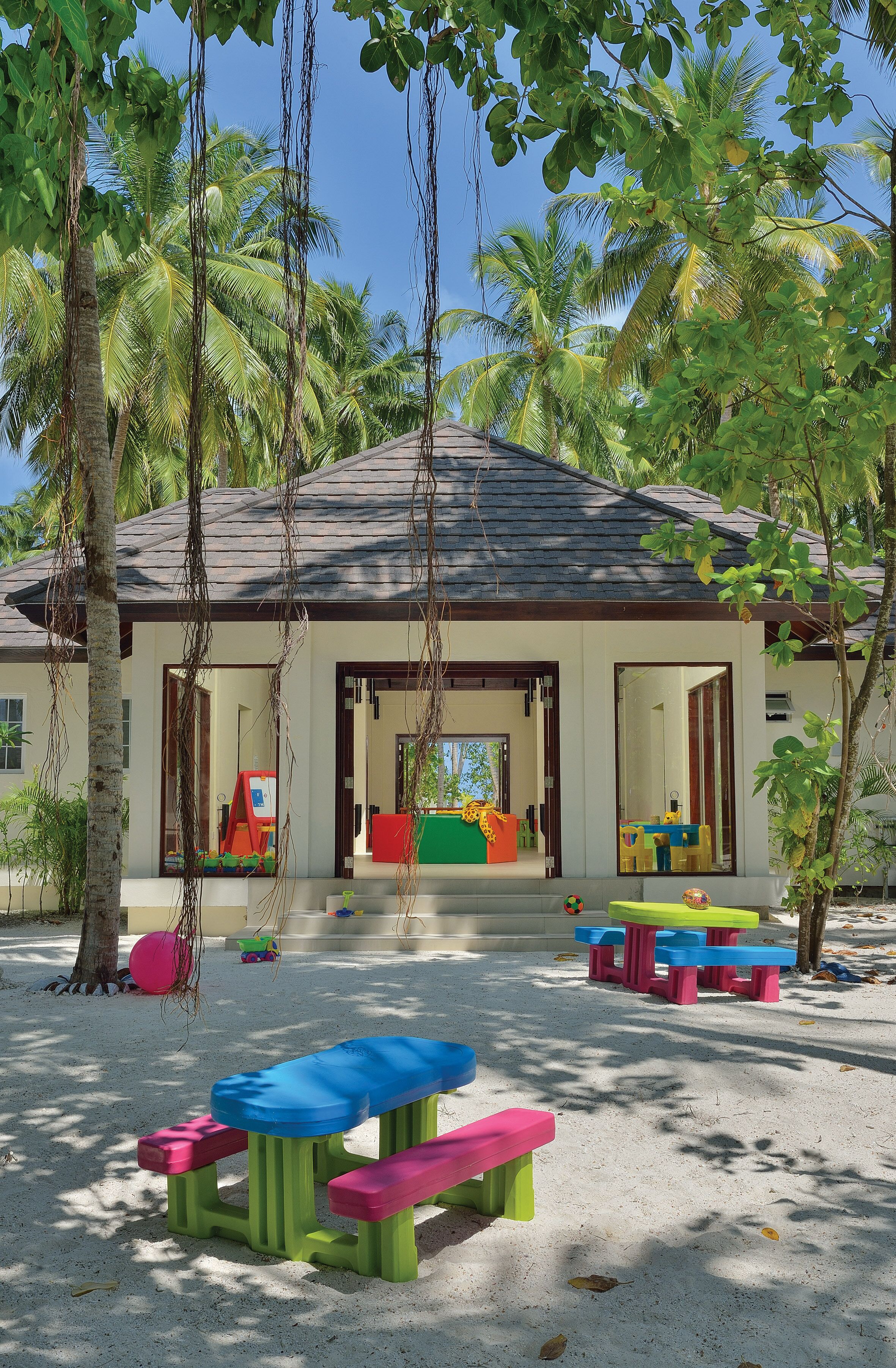 A beachside building with a covered patio area, colorful play tables, and palm trees.
