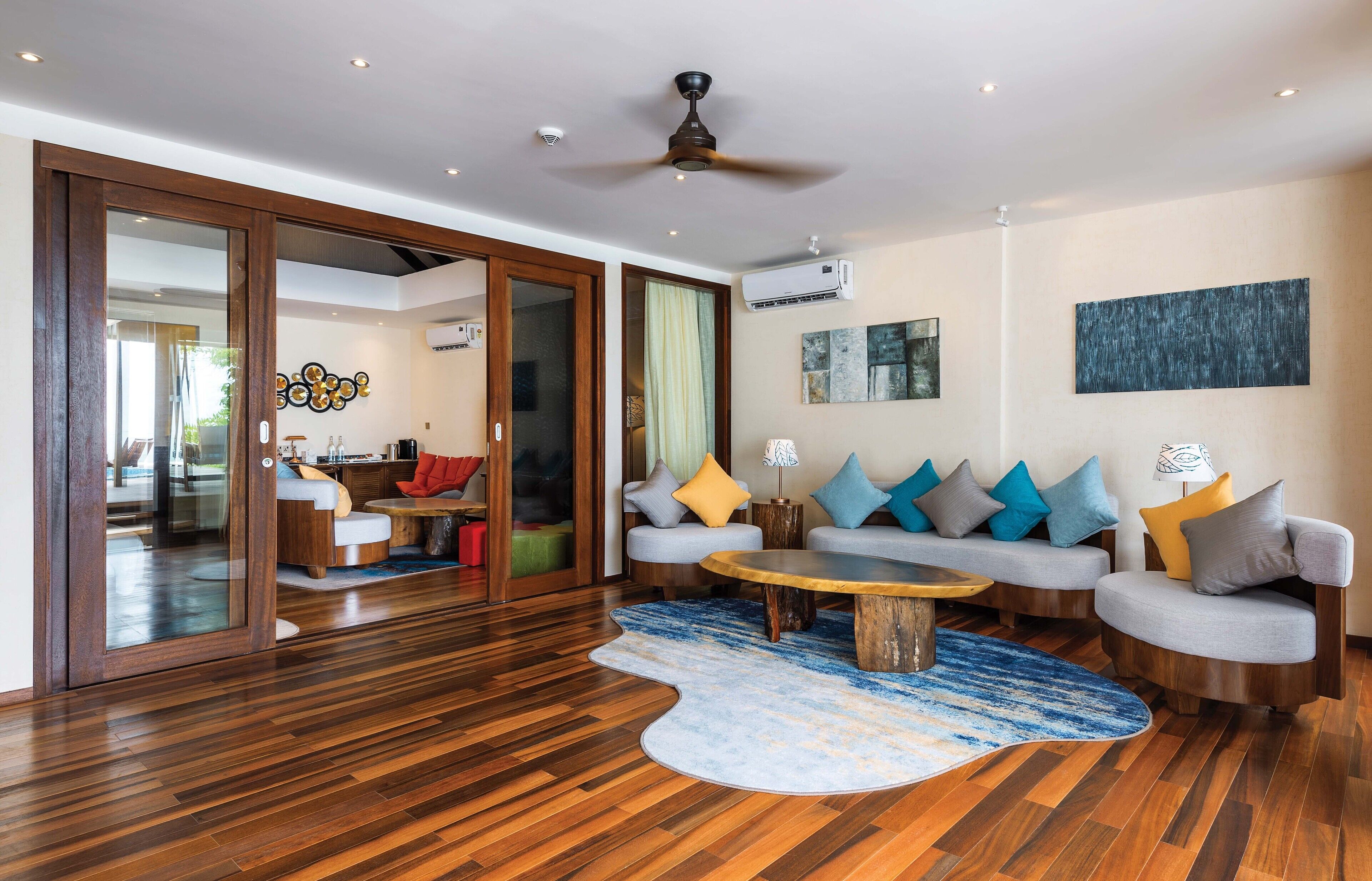 Una sala de estar moderna con piso de madera, una mesa de centro redonda y dos sofás grises con cojines coloridos.