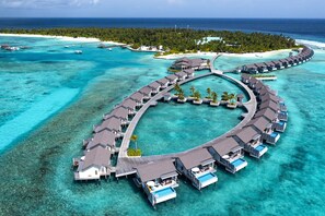 An overwater resort with multiple bungalow-style accommodations connected by walkways, surrounded by clear turquoise waters and a backdrop of a tropical island. - Atmosphere Kanifushi - Premium All Inclusive with Free Transfers (Kanifushi (Lhaviyani Atoll))