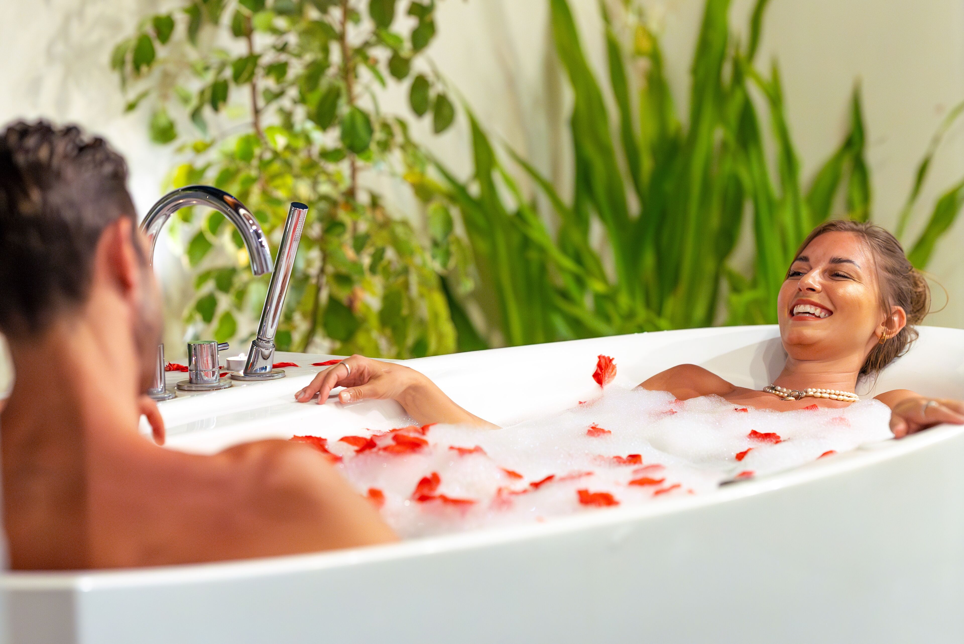 Eine Wanne mit Rosenblättern, einem Wasserhahn und einer Pflanze im Hintergrund.
