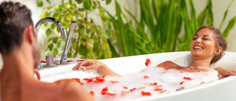 A bathtub with rose petals, a faucet, and a plant in the background.