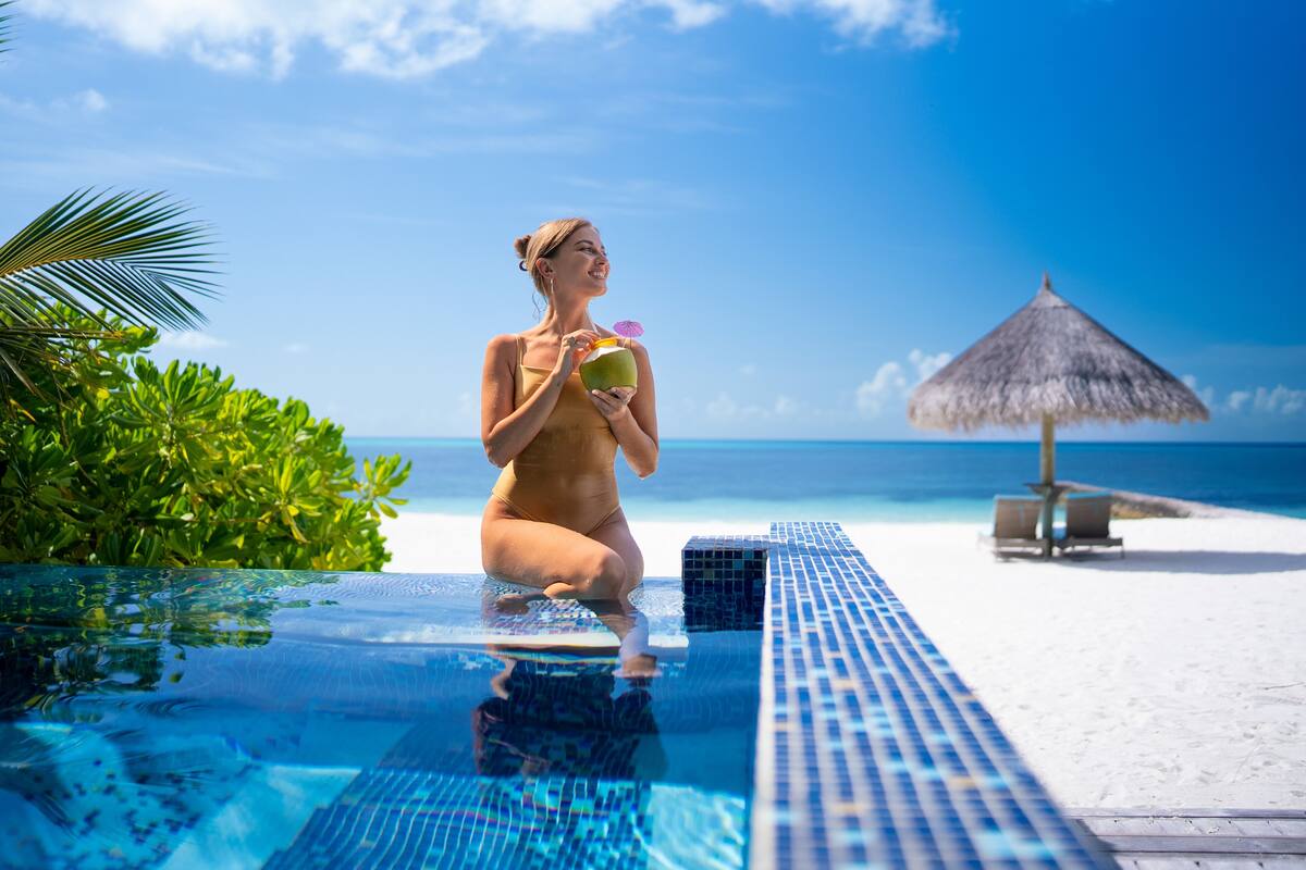 Eine Person im Badeanzug an einem Pool mit Strand und Meer im Hintergrund.