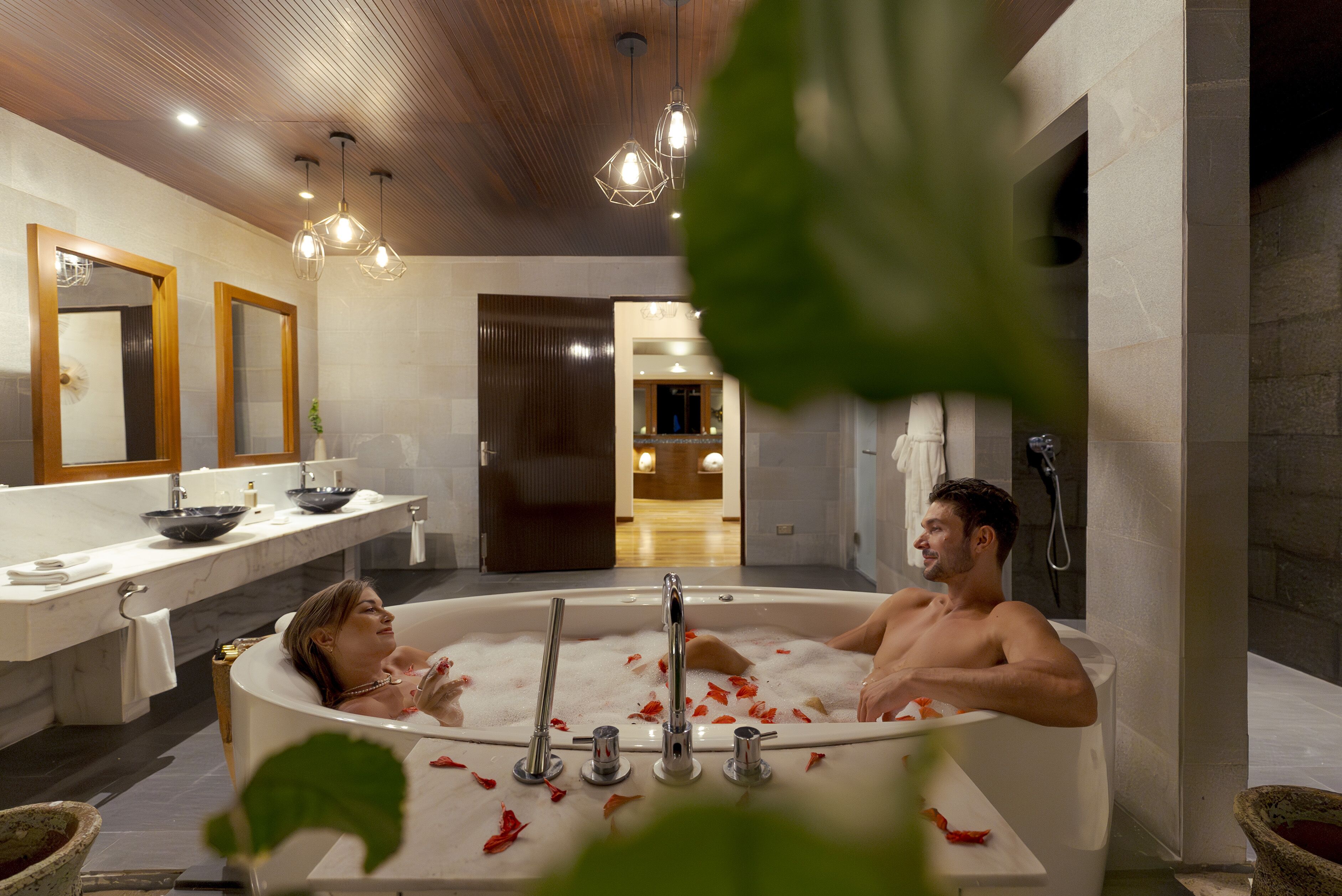 A modern bathroom with a large bathtub, dual sinks, and a wooden ceiling.