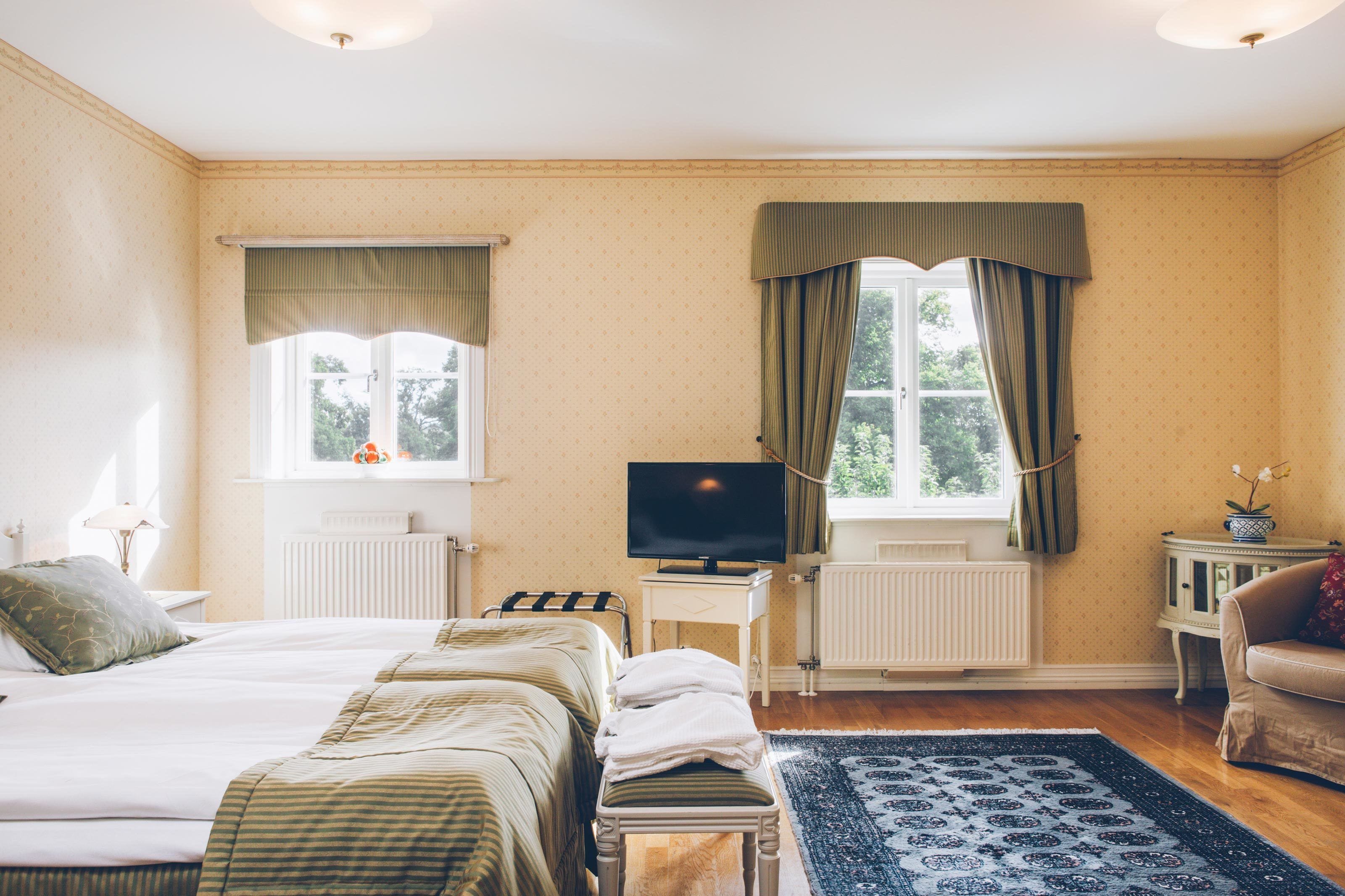 Et hotelværelse med seng, fjernsyn, et lille bord, en stol og et vindue med gardiner.