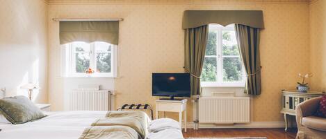 Habitación de hotel con cama, televisión, mesita, silla y ventana con cortinas.