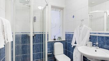 A bathroom with a glass-enclosed shower, a white toilet, a sink with a marble countertop, and a window with a decorative view.