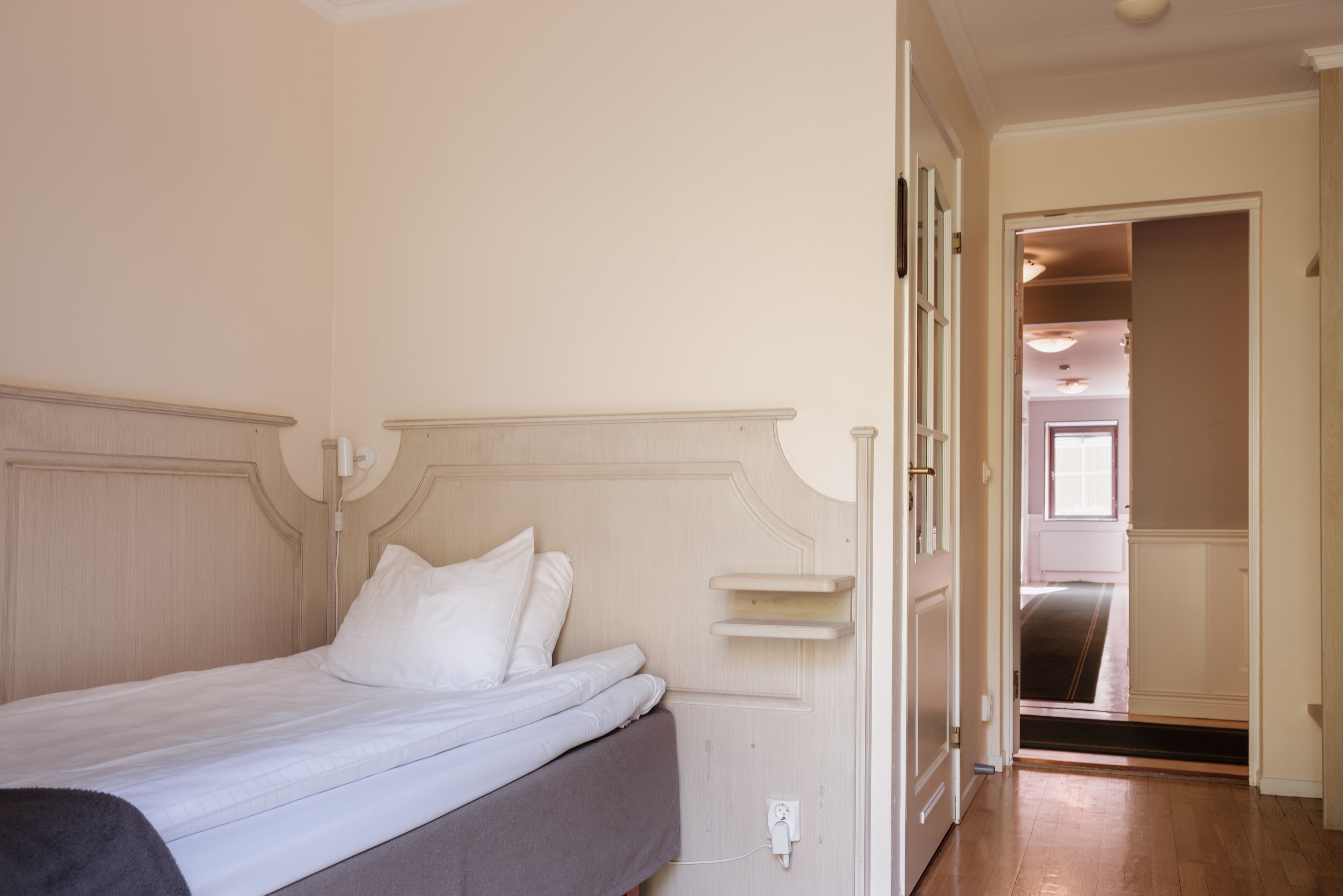 Un dormitorio con una cama, una mesita de noche y una puerta que da a otra habitación.