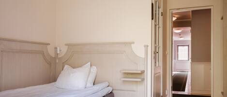 Un dormitorio con una cama, una mesita de noche y una puerta que da a otra habitación.
