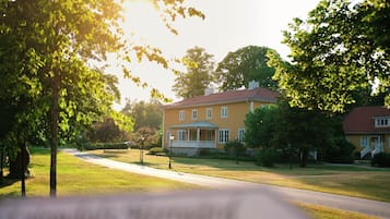 A two-story yellow house with a red roof, surrounded by trees and a well-maintained lawn.