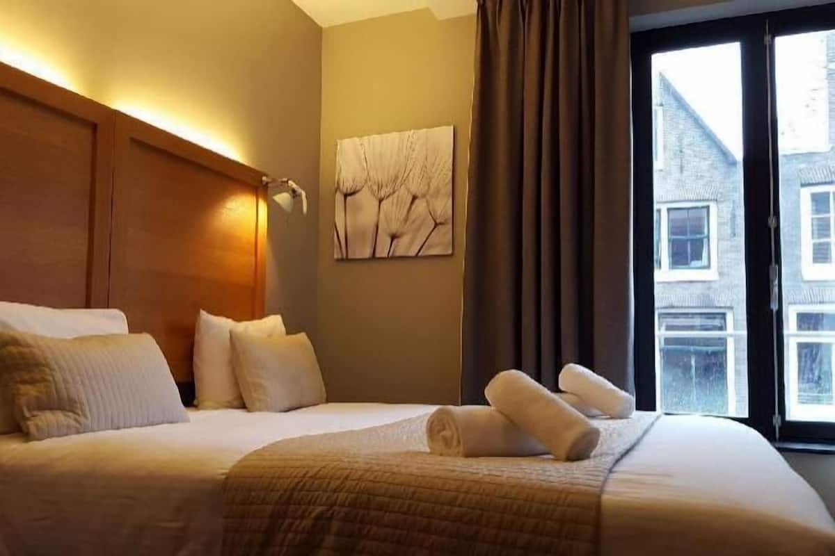 A hotel room with a large bed, a headboard, a wall-mounted artwork, and a window with curtains.