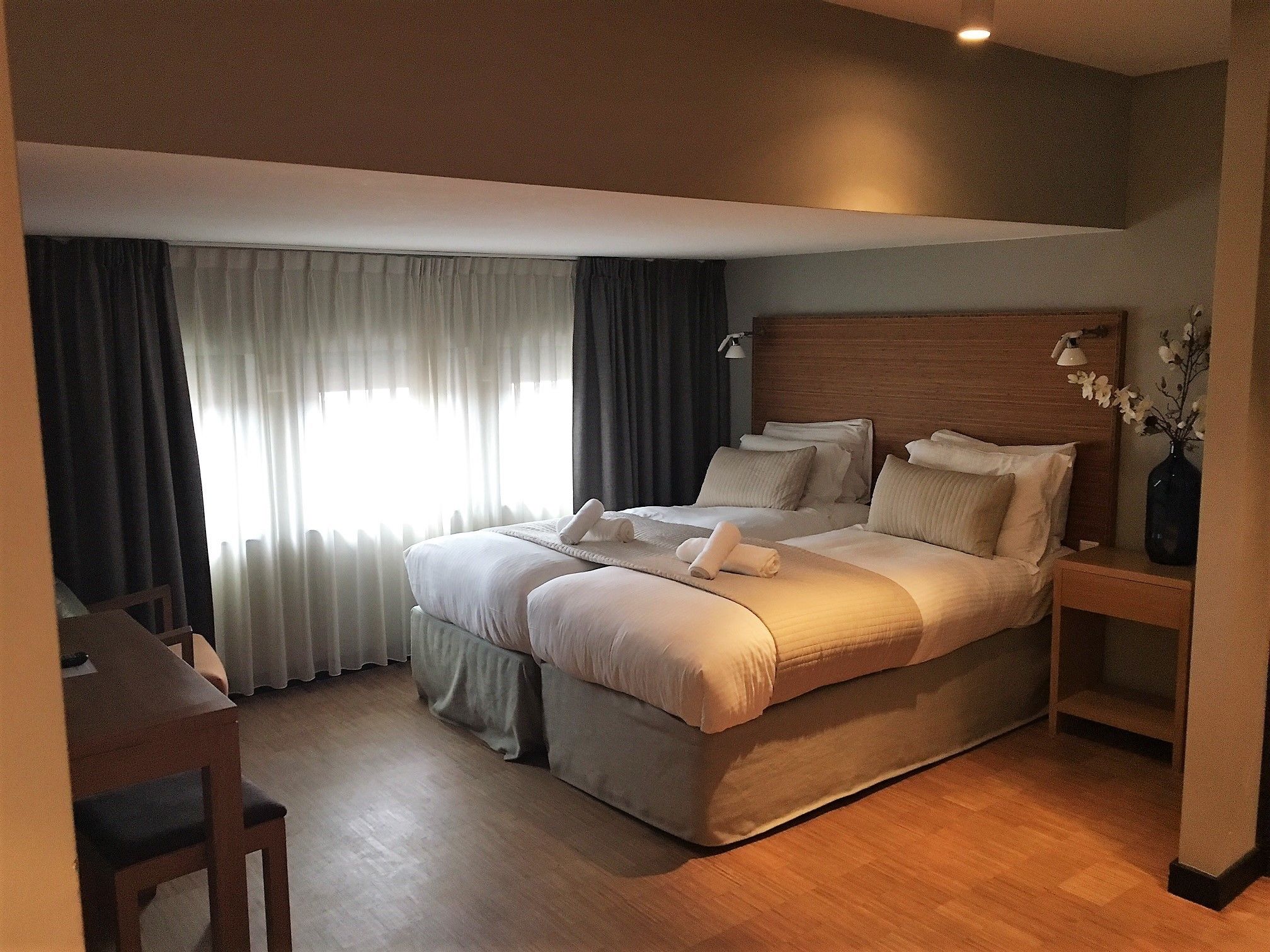 Habitación de hotel luminosa con una cama grande, una mesita de noche y una silla.