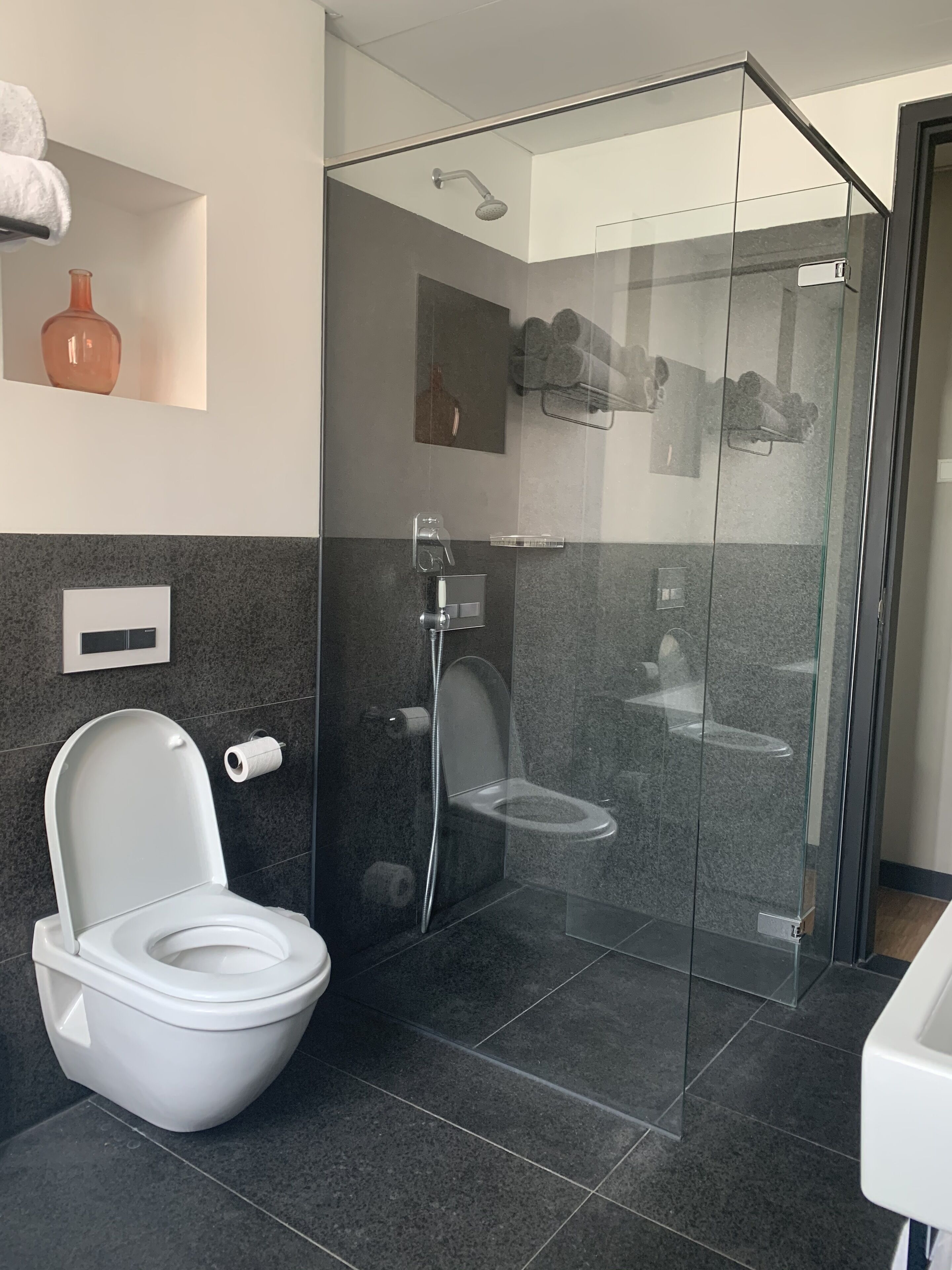 A modern bathroom with a glass-enclosed shower, a white toilet, and a marble-tiled floor.