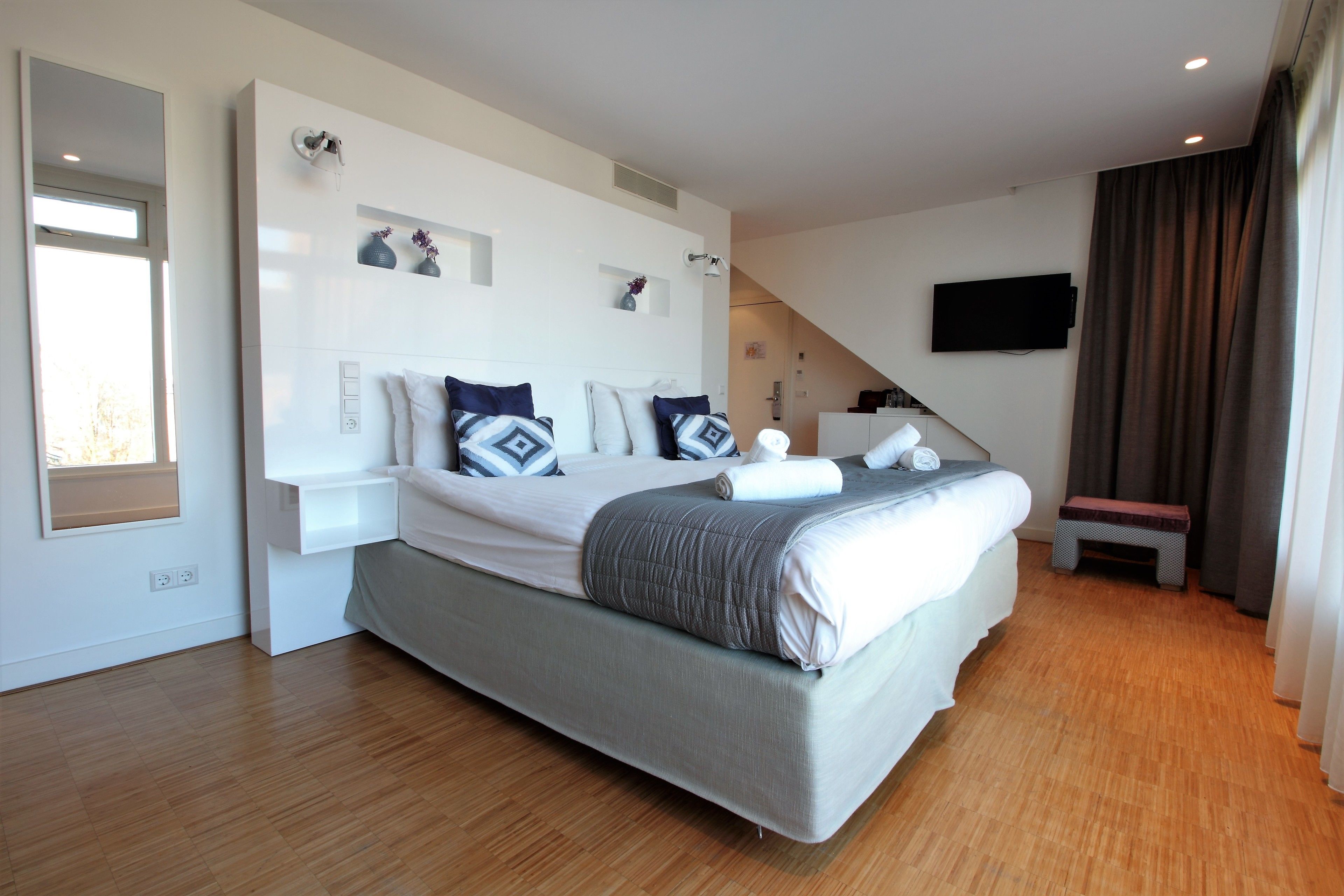 A modern bedroom with a large bed, bedside tables, a flat-screen TV, and a window with curtains.