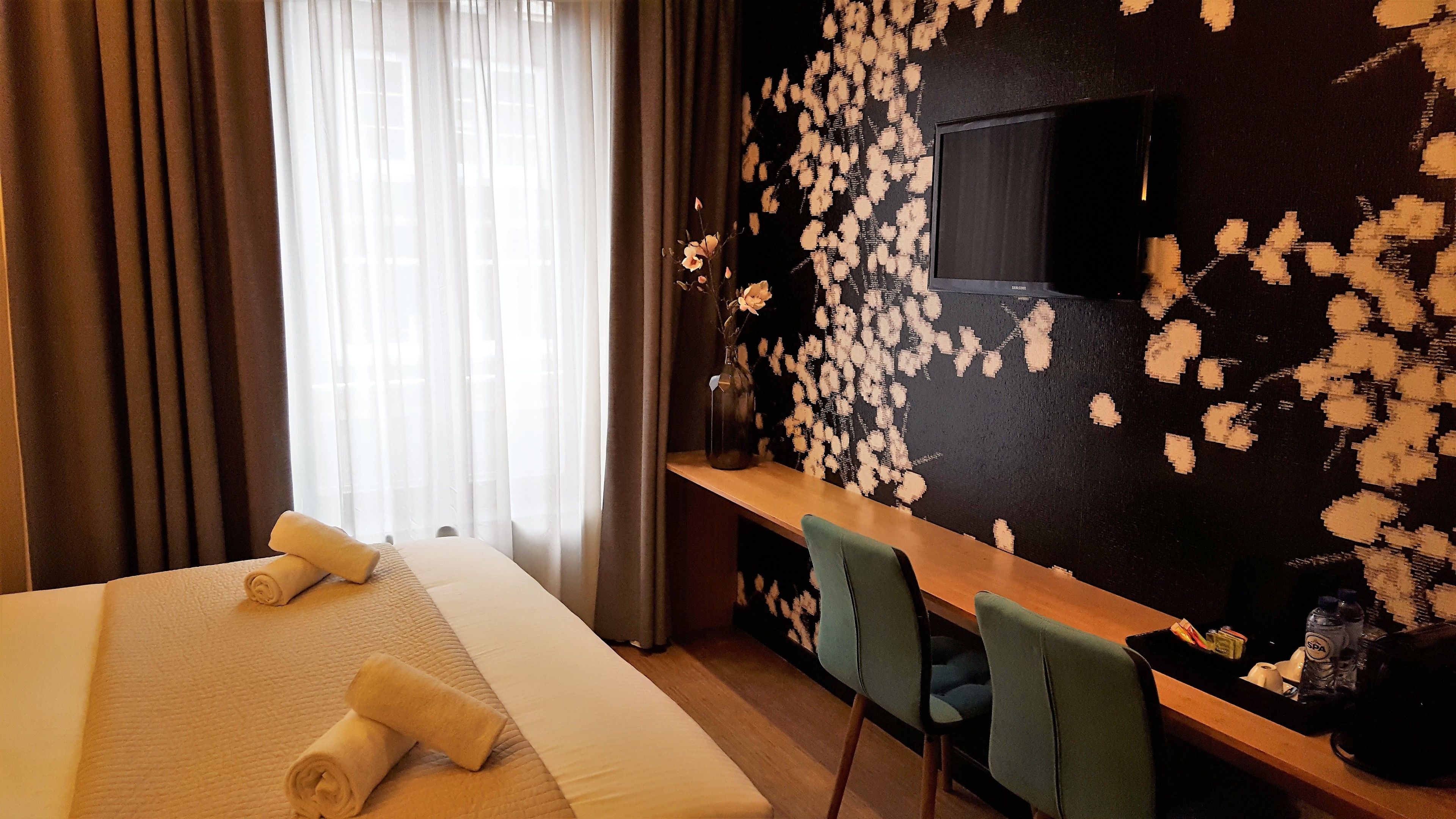 Ein Hotelzimmer mit einem großen Bett, einem Schreibtisch mit Stuhl, einem Fernseher und einer Wand mit Blumenmuster.