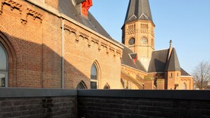 Een ronde tafel met een kopje en schotel, met daarin de reflectie van een gebouw met een klokkentoren en bakstenen muren.