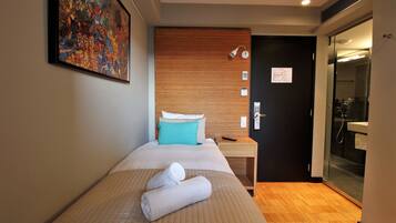 A hotel room with a bed, a wooden headboard, a painting on the wall, a nightstand, a bathroom with a glass door, and a map on the door.